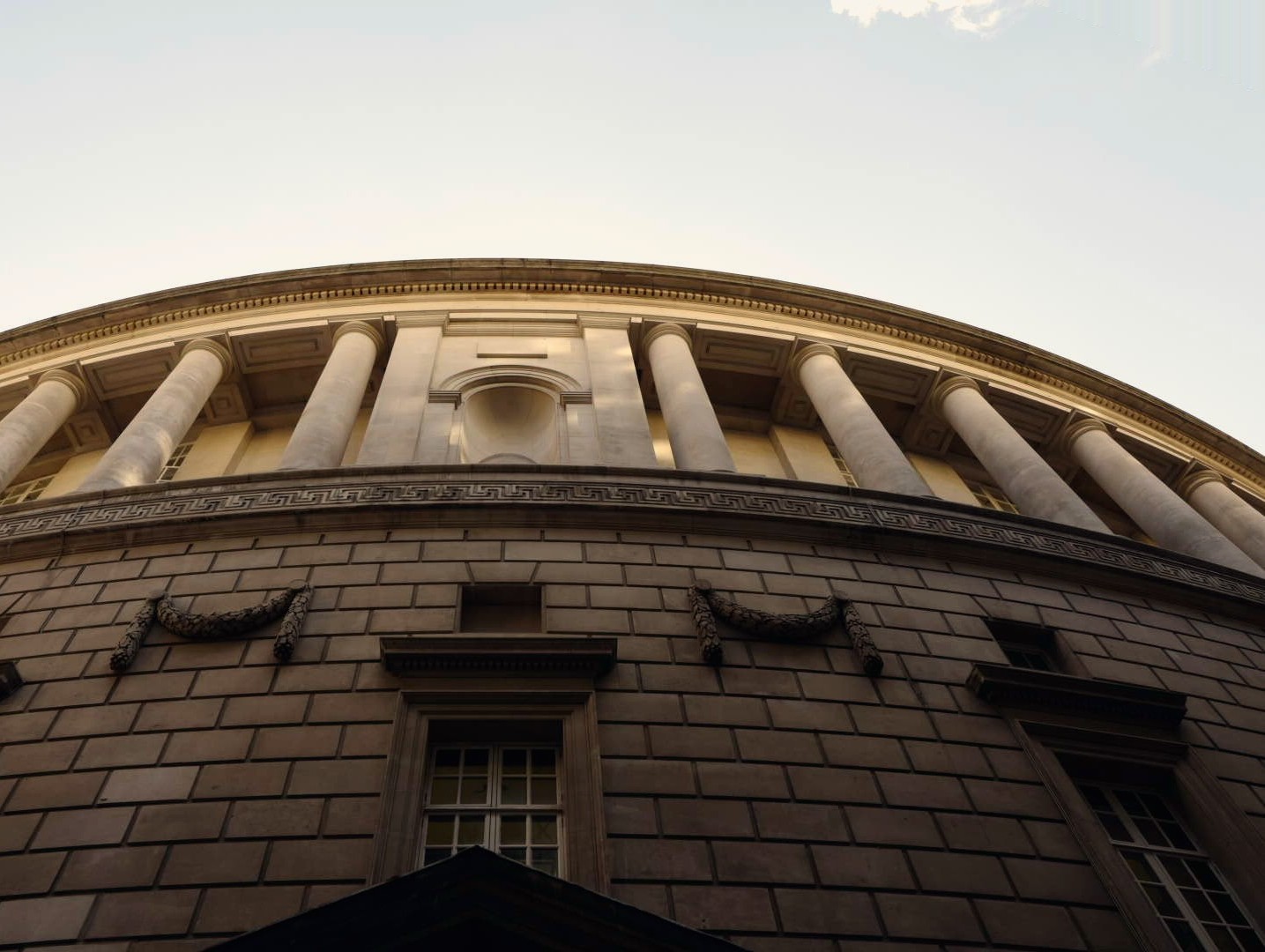 The curved neoclassical colonnade of Manchester Central Library, seen from below against a pale sky.